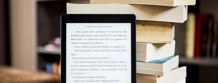 An e-reader displays text next to a stack of books.