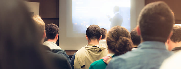 A crowd of people facing a screen during a presentation.