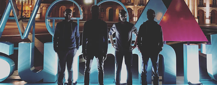 Four people silhouetted in front of a large illuminated "SUMMIT" sign at night.