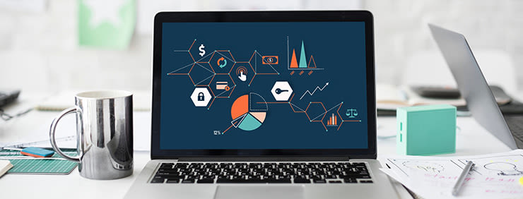 A laptop showing infographics with hexagonal shapes on a blue screen, placed next to a silver mug, a blue cube, and papers with sketches.