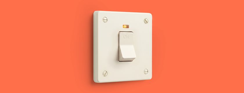 A white light switch in the on position is mounted on a coral-orange background, with a small amber indicator light glowing above it.