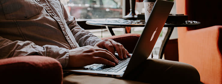 A person sitting in an orange chair using a laptop, with a small round table and drink visible in the background.