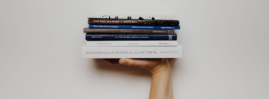 A stack of books held up by a hand, with titles visible on the spines.