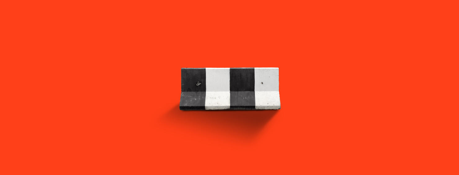 A black and white striped concrete barrier stands against a bright red background.