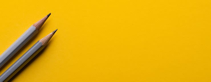 Two gray pencils lying on a bright yellow background.