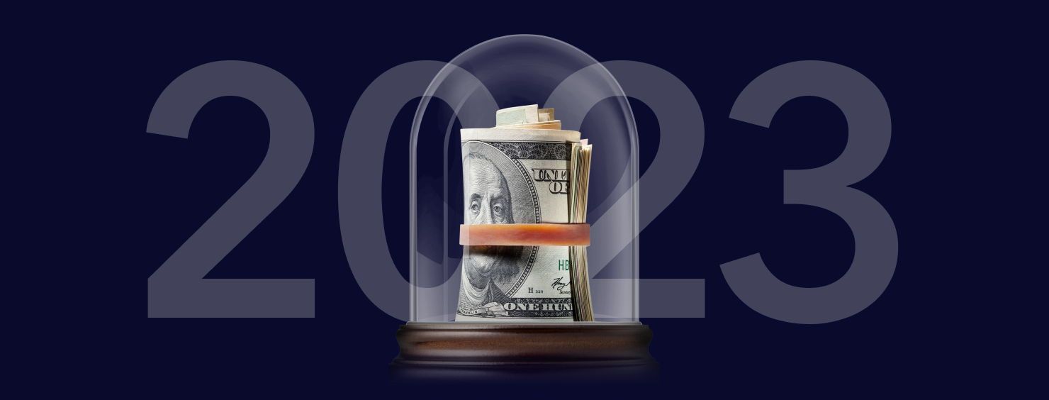 "2023" text overlaying a roll of US currency, secured with a band and displayed under a glass dome. The background is a dark blue.