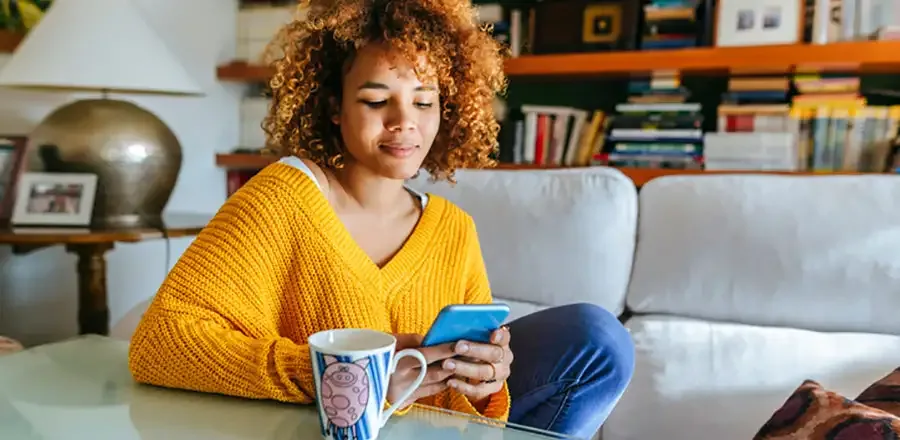 Teenage girl with a smartphone in her hand drinking tea