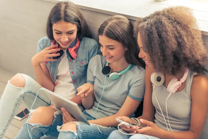 Three smiling teenage girls sitting against the wall with tablet