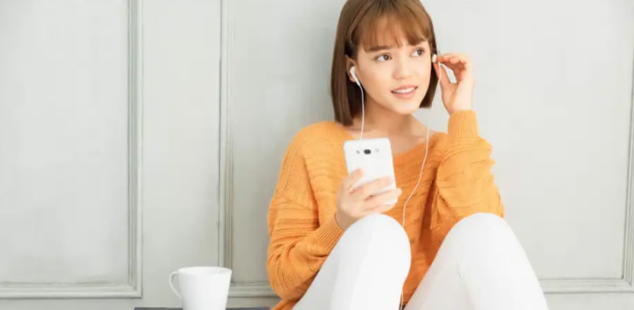 Teenage girl with headphones using mobile phone while sitting against a wall