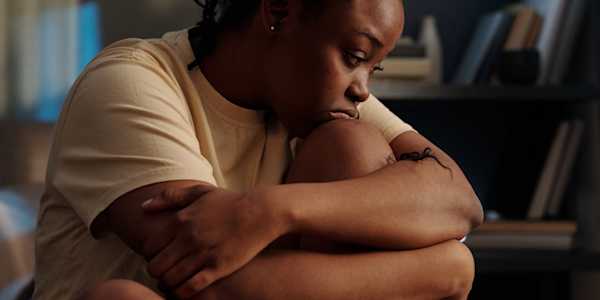 Woman looking sat and sat hugging her knees