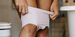 Person lowering their underwear in a bathroom, representing bowel habits and toileting.