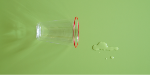 Um copo tombado e um respingo de água próximo a ele em uma superfície verde.