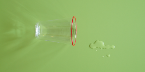 Un verre renversé et une éclaboussure d'eau à côté sur une surface verte.