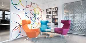 A photo of the Clue office space showing a colorful wall decorated with the Clue logo, a bookshelf, and three armchairs. 