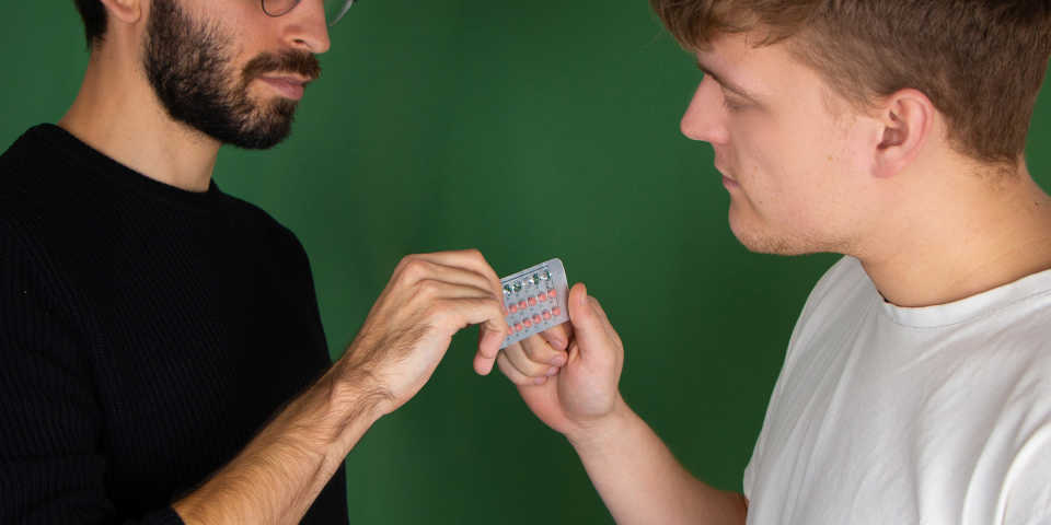 Two men with a pack of birth control pills