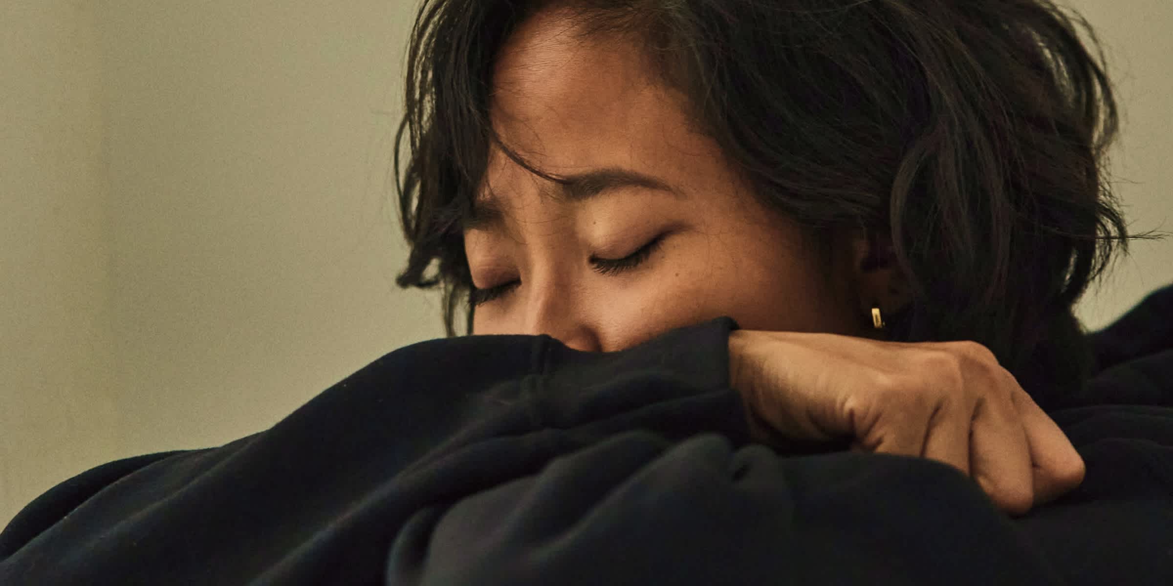 Eine verzweifelte Frau in einem schwarzen Pullover, die ihr Gesicht mit den Händen bedeckt, mit dem Logo der Clue App in einer Ecke.
