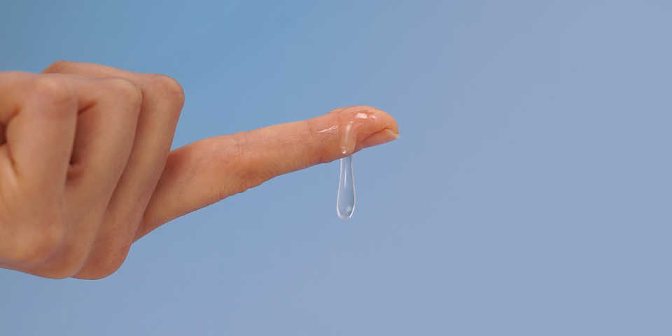 A hand with the index finger extended with a large dollop of personal lubricant dripping off the side.