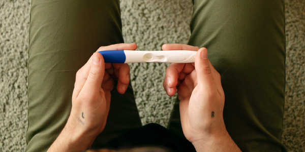 Photograph of Elliot holding a pregnancy test in their hand