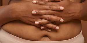 A person's interlaced fingers are placed over their abdomen.