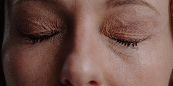 Imagem de uma mulher com os olhos fechados, demonstrando dor.