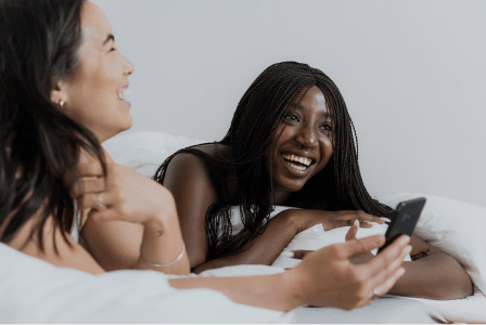 an image of two people lying on a bed looking at a phone