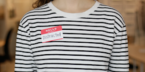 close up photograph of a woman wearing a striped shirt and a stickers saying hello my name is distracted in front of a blurry background