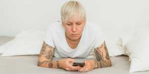 A person with short blonde hair frowns while looking at their phone.