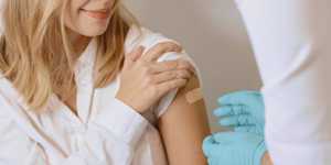 woman after getting a vaccine with a plaster covering her upper arm and a doctor wearing gloves