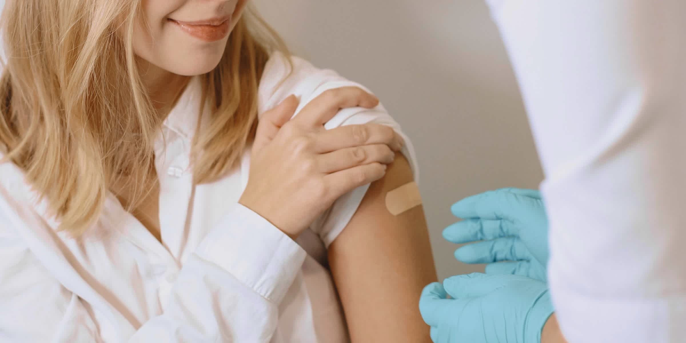 woman after getting a vaccine with a plaster covering her upper arm and a doctor wearing gloves
