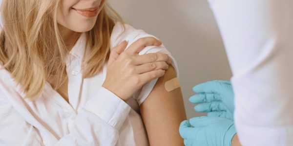 woman after getting a vaccine with a plaster covering her upper arm and a doctor wearing gloves