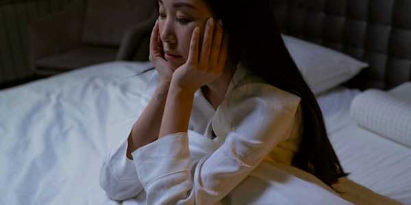 Woman sitting up in bed with her head in her hands