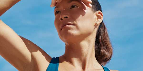 Woman outside with a blue sky in the background, sun on her face and hand shielding her eyes