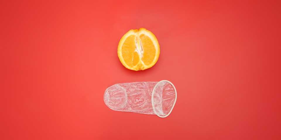 Um preservativo feminino desempacotado, mostrado ao lado de uma laranja para uma perspectiva do tamanho.