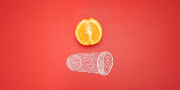 Ein ausgepacktes weibliches Kondom, das neben einer Orange für die Größenperspektive gezeigt wird.