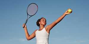 Woman athlete holding a tennis racket in one hand and a tennis ball in the other going to serve