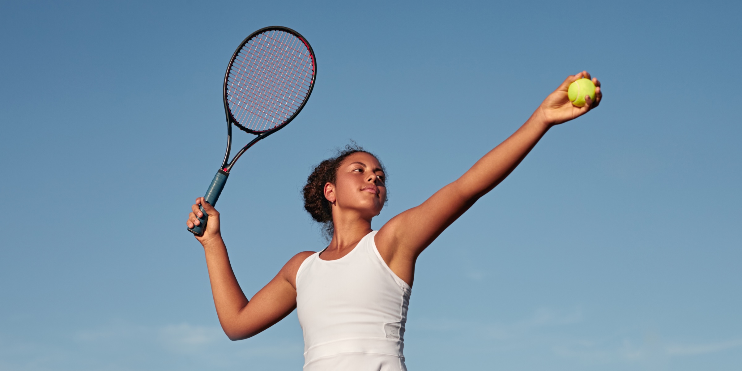 Woman athlete holding a tennis racket in one hand and a tennis ball in the other going to serve