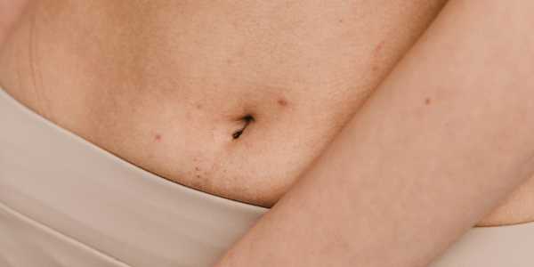 Close-up of a person's lower abdomen and belly button above a beige waistband, with an arm resting across their body.
