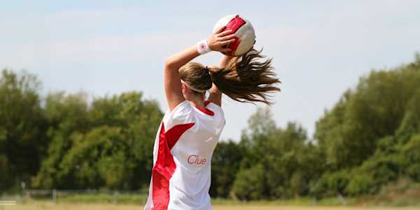 woman holding a football in both hands above her head and wearing a white t-shirt with the Clue logo on the back