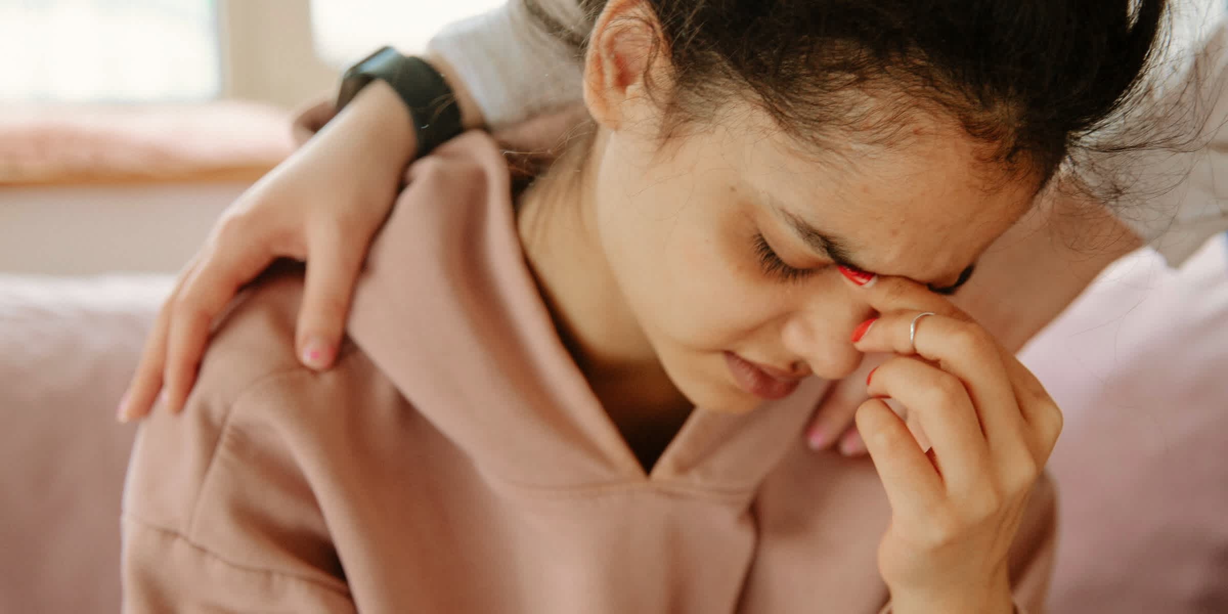 A woman in a hoodie pinching the bridge of her nose in frustration or pain