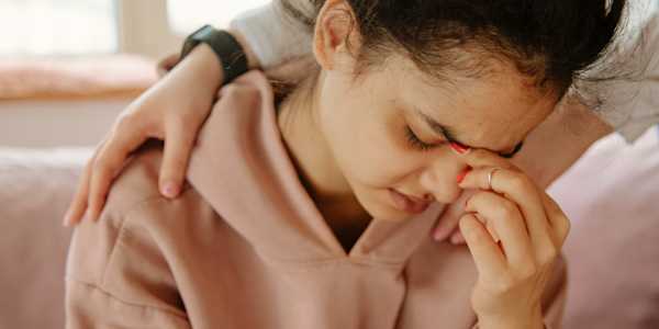A woman in a hoodie pinching the bridge of her nose in frustration or pain
