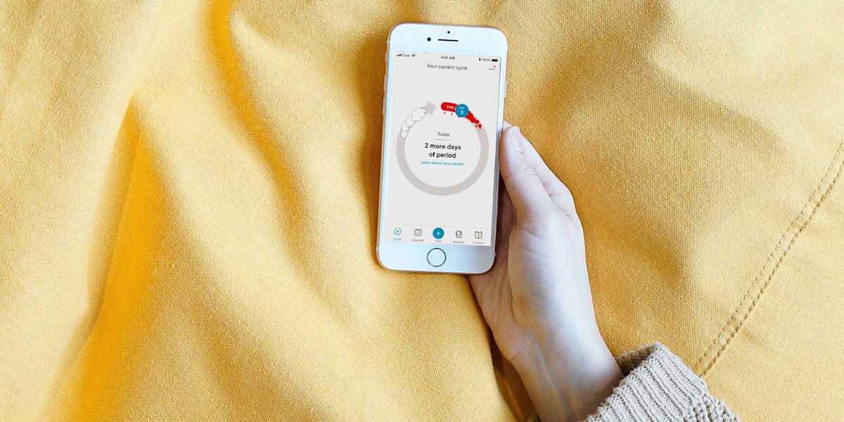 An image of a white person's hand holding a smartphone with Clue's cycle view visible.