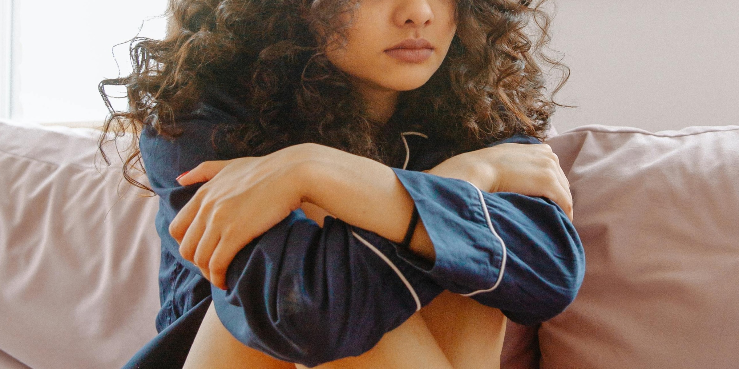 A woman with curly hair sat on a sofa, hugging her knees to her chest