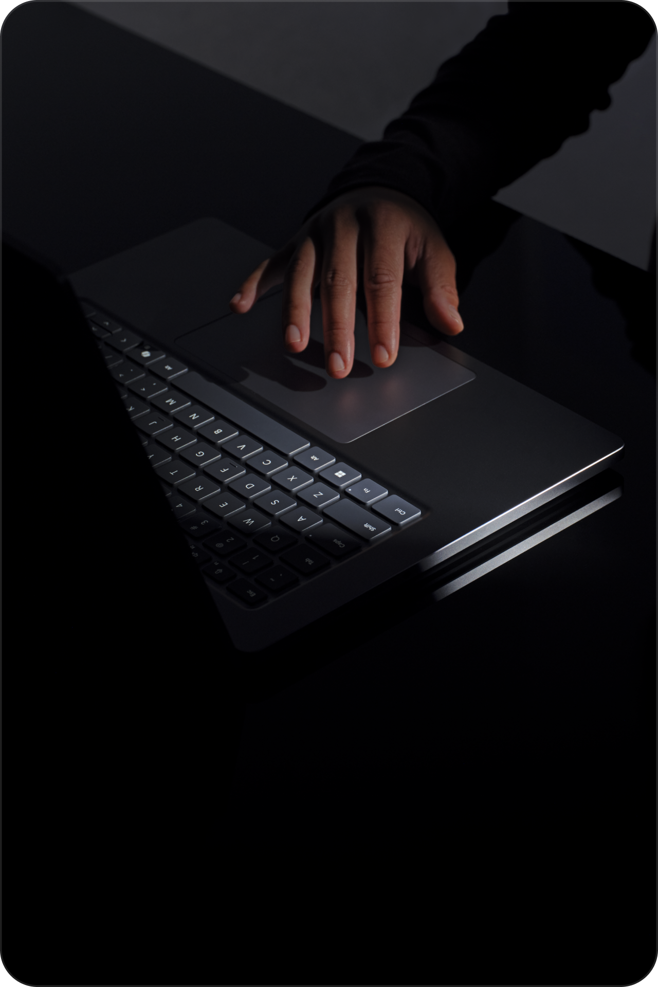 Close-up of a hand using the trackpad on a Microsoft Surface laptop in low light