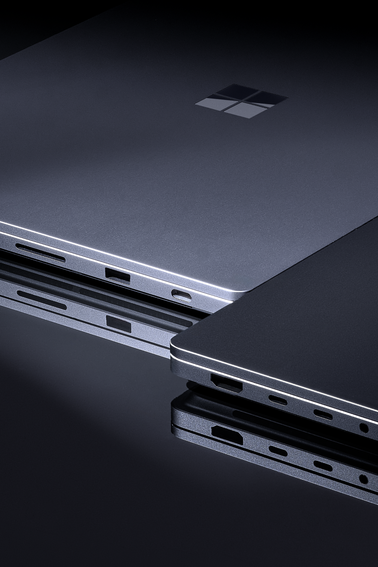 Gros plan d’ordinateurs portables Microsoft Surface empilés montrant les ports latéraux et la conception mince en aluminium sur une surface réfléchissante