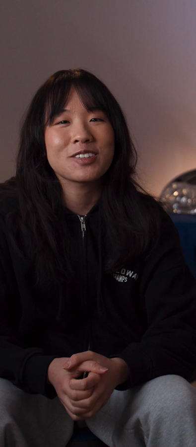 Person seated in a garage in front of a blue car with the hood open, speaking on camera about using a Surface Laptop for working on the go