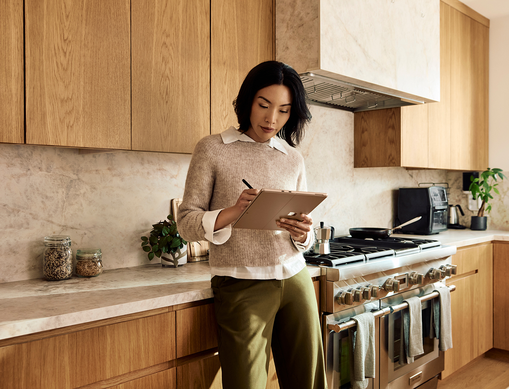 Woman in kitchen using a digital pen on her Surface Pro device.