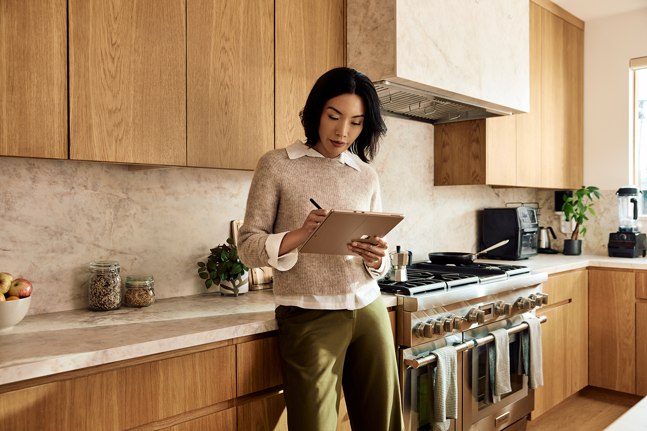 キッチンで Surface Pro デバイスにデジタル ペンを使っている女性。