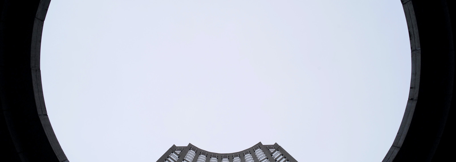 Image looking up towards a tall corporate tower through a circular building