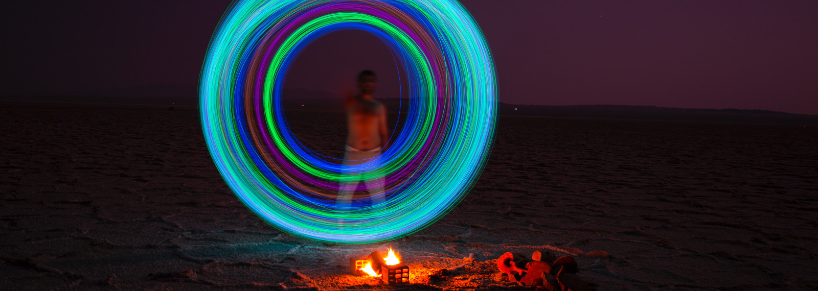 image of an illuminated circle above a camp fire and in front of a figure