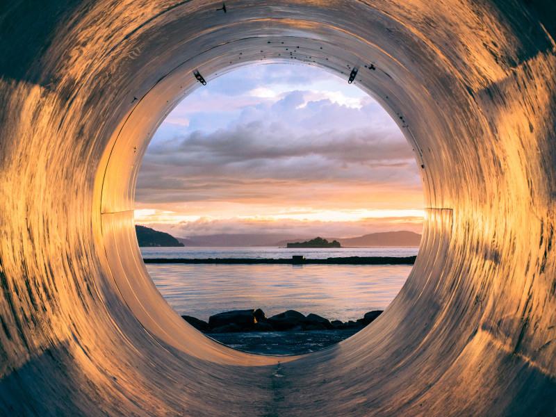 Image looking out at a waterscape through a circular tunnel